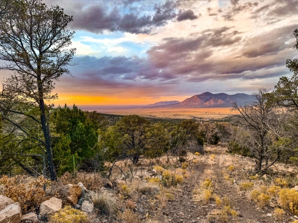 Picturesque view of Rancho Vista Del Valle at Sunset, with hillside foliage and road access leading to vibrant orange-violet clouds over mountain peaks